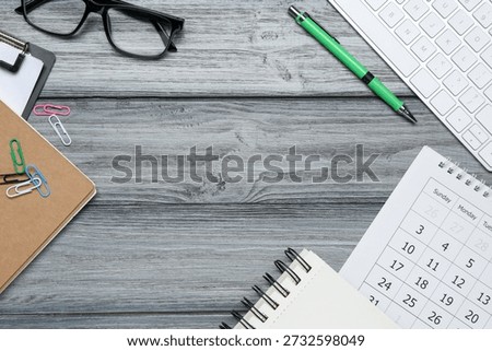 Office workplace. Computer keyboard, glasses and stationery on grey wooden desk, flat lay. Space for text
