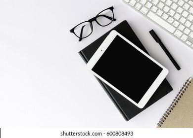 Office workplace with text space, White wooden table with office supplies tablet, desktop computer and book, top view, over light