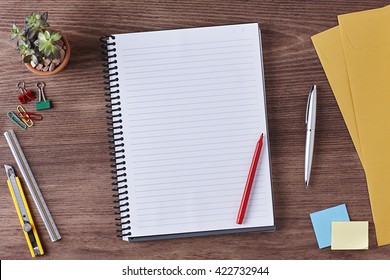 Office Workspace. Top View of a Business Workplace. Wooden Desk Table, Paper Cutter, Ruler, Pen, Pencil, a Blank Notebook, Envelope, Red Pen, Plant Pot, Clips. Copy space for text or Image