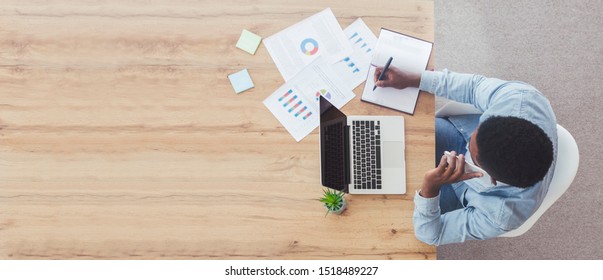 Office Workspace Top View. Busy Businessman Working At Wooden Desk Using Laptop, Talking On Phone And Taking Notes, Panorama With Copy Space