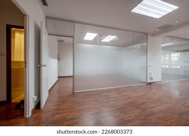Offices of an empty office with technical ceilings, glass partitions and reddish floating flooring