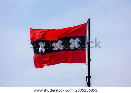 Official flag of Amsterdam waving on the air in a sunny day and blue sky background, The flag depicts three Saint Andrew's Crosses and is based on the escutcheon in the coat of arms of Amsterdam.