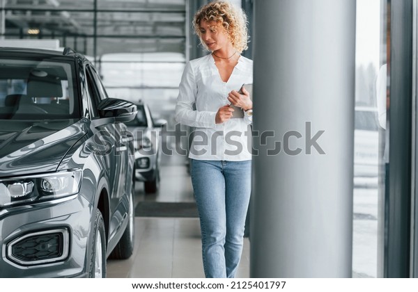 In official white shirt. Woman with curly\
blonde hair is in autosalon.