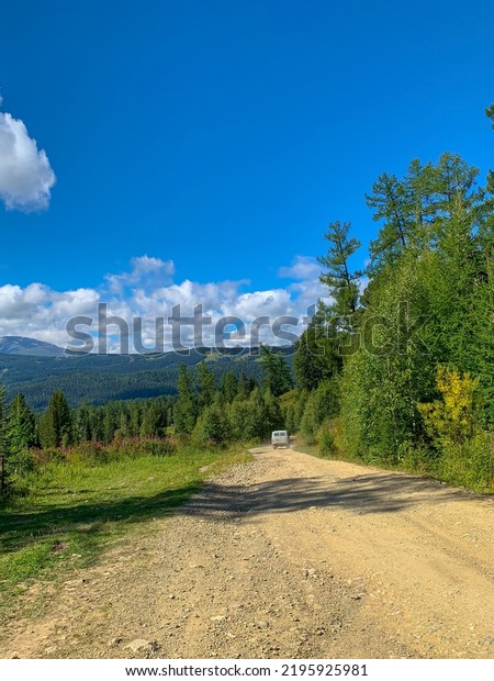 An off-road car drives along a dirt road along the\
forest to the mountains. Photos of the Republic of Gorny Altai in\
summer, Russia