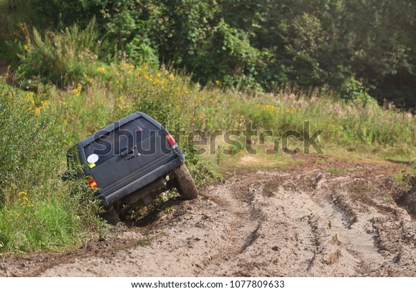 An off-road car flew to the\
side of the muddy road on a sunny day. Concept with offroad\
wheel.