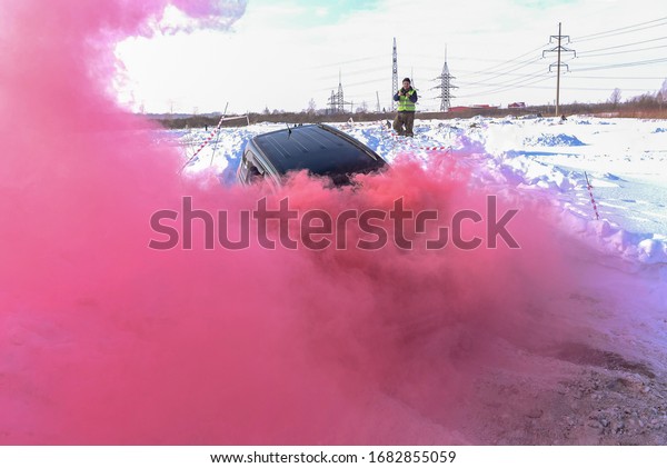 An off-road car slides down a mountain in strong\
multi-colored crimson smoke against the background of a man with a\
photo of a mobile gadget.