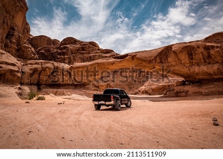 Off-road car in view through a rock arch in the desert of Wadi Rum. Jordan