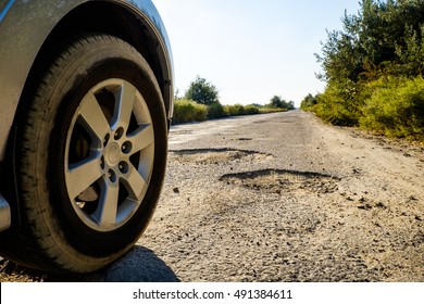 Off-road Car Wheels On Damaged Road, Cracked Asphalt Blacktop With Big Holes, Ukraine. Tire On Bad Tarmac Road. Outdoor, Adventures, Expedition, And Travel Suv. Close-up Car Tyre Tracks.