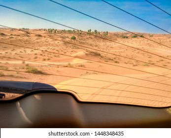 Off-road Safari On SUVs In The Arab Orange-red Sands Desert In The Sunset Sun. The Picture Through Rear Screen Of The Car. From The Inside The Car. On Background The Desert And Rare Bushes.