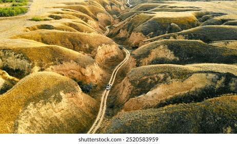 Off-Road Vehicle in Desert Canyon. An aerial view of an off-road vehicle driving through a rugged desert canyon with steep, eroded hills. - Powered by Shutterstock