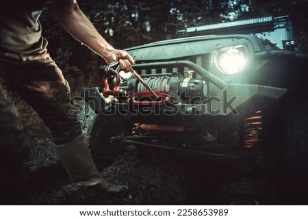 Off-Road Vehicle Got Stuck in the Mud During Recreational Ride. Driver Assistant Unrolling the Winch to Help Pull the Car Out. Muddling in the Forrest.