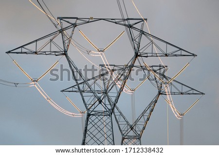 Offset select focus of brilliant sunlight reflecting from electrical power lines strung between two high tension towers against a partly cloudy sky at sunset