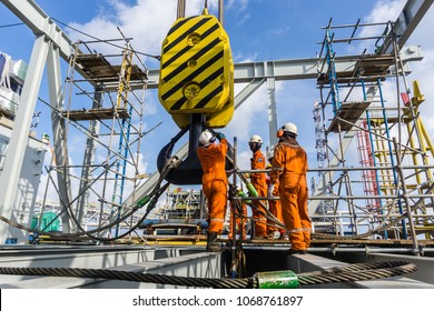 Offshore construction workers handling sling onto crane hook prior to heavy lifting on a construction barge at oil field