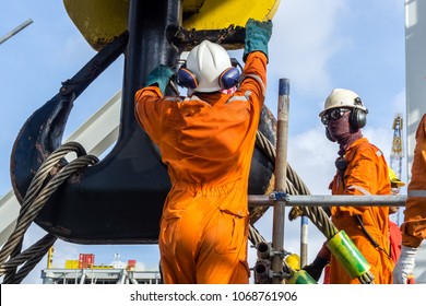 Offshore construction workers handling sling onto crane hook prior to heavy lifting on a construction barge at oil field