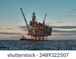 Offshore oil and gas jackup platform, during cargo operations with supply vessel in the sea and beautiful colourful sunset sky. 