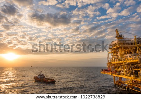 Offshore oil and Gas processing platform, petrolium industry to treat raw gases and sent to onshore refinery with supply boat in sunset time.