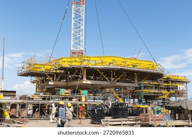 Offshore platform under construction lifted by towering crane. Steel structure, mechanical systems installed at oil gas energy site. Represents heavy industry, engineering and energy sector investment