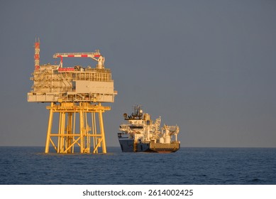 Offshore Substation Platform and SOV Vessel in DP Mode, Wind Farm Construction Site During Golden Hour