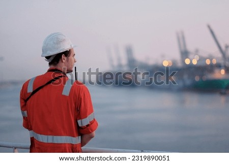 Offshore technician. Seafarer. Seaman. Navigator. A man in a boiler suit is standing in front of the port. Seafarer in front of the container terminal.
