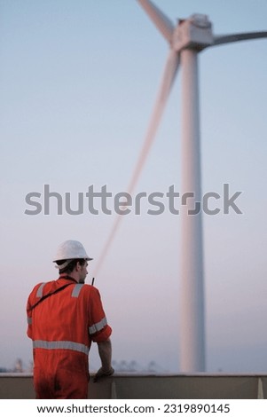 Offshore technician. Seafarer. Seaman. Navigator. A man in a boiler suit is standing in front of the wind generator. Seafarer in front of the wing generator. Wind generator technician.