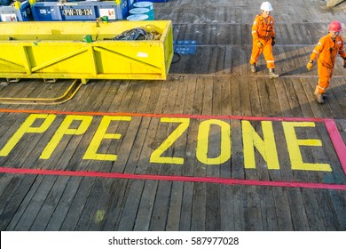 Offshore Terengganu, Malaysia. August 2015. Offshore workers walking on a main deck of a construction barge with signage 'Full PPE Zone' on the wooden deck at oilfield Terengganu, Malaysia