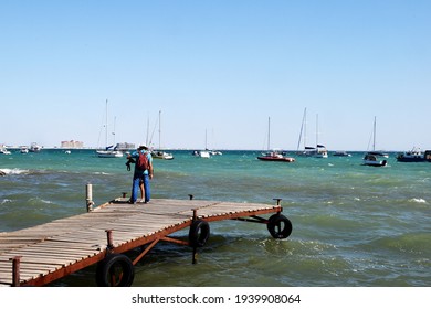 Offshore, there are many different private yachts anchored. Two, a man and a woman, famous tourists, stopped at the pier and sorted out the camera.