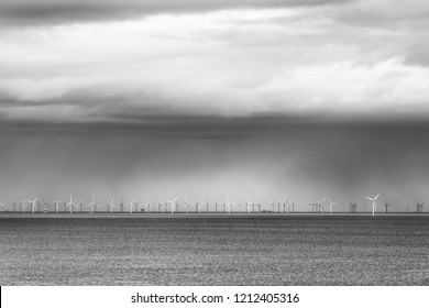 An Offshore Wind Farm On The Ocean Beneath A Stormy Sky. 