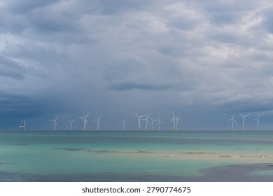 Offshore wind turbines beneath dramatic storm clouds above the turquoise waters of Aewol-eup on Jeju Island, South Korea.