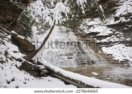 Often called buttermilk falls, this waterfall is located in Cuyahoga Valley National park. It is a cold winter day, and snow covers the hemlock and other evergreens nearby.