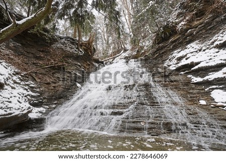 Often called buttermilk falls, this waterfall is located in Cuyahoga Valley National park. It is a cold winter day, and snow covers the hemlock and other evergreens nearby.