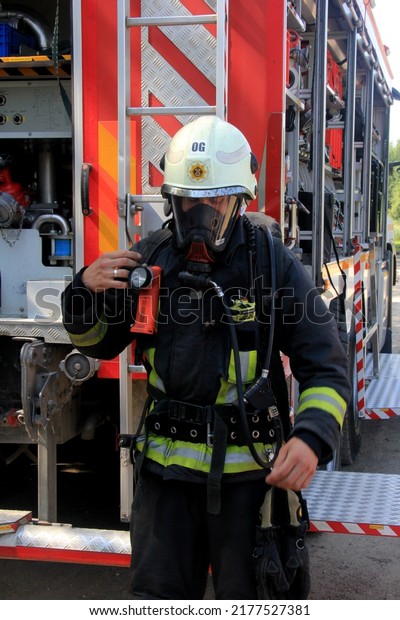 Ogre, Latvia, June 28 2022: A firefighter in\
full gear stands by a fire truck. A red fire truck at the scene of\
an emergency