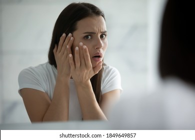 Oh god, a pimple! Anxious worried girl teenager or millennial woman watching herself in big mirror troubled by bad condition of facial skin acne wrinkles freckles sunspots oily irritated problem skin