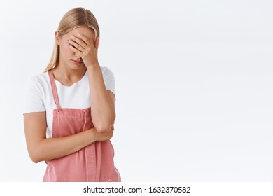 Oh gosh why me. Embarrassed and tired young annoyed blond girl, do facepalm, hold hand on face, trying calm down as being irritated and pissed, standing uneasy over white background - Shutterstock ID 1632370582