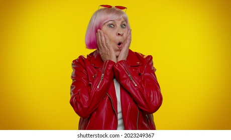 Oh my God wow. Excited amazed elderly rocker woman with pink hair raising hands in surprise looking at camera with big eyes, shocked by sudden victory. Senior old punk grandmother. People emotions