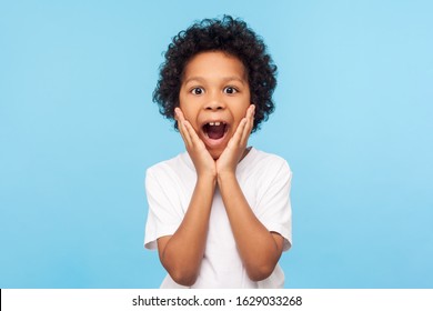 Oh My God, Wow! Portrait Of Funny Amazed Preschool Boy Looking At Camera With Shocked Astonished Expression And Keeping Hands On Face, Screaming In Surprise. Studio Shot Isolated On Blue Background