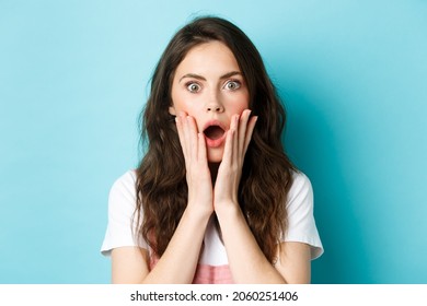 Oh my gosh. Close up portrait of shocked girl face, touching head and staring at camera startled, hear bad news, standing over blue background