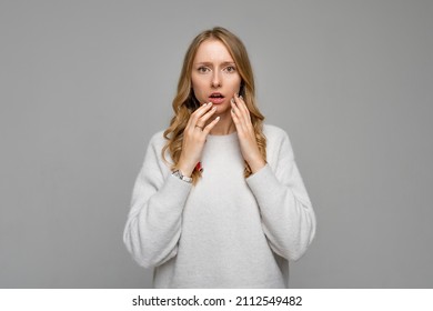 Oh no, it is bad. Portrait of worried woman with dropping jaw and holding hands near her face, frowning, feeling anxious or nervous while being in danger, gray background