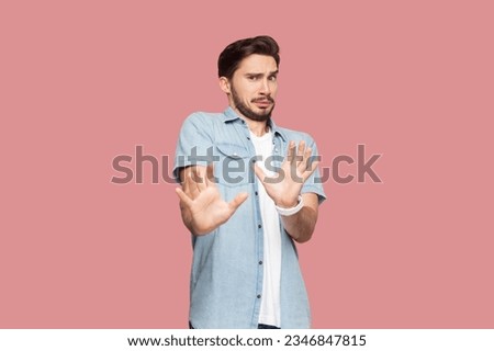 Oh no, stop it immediately. Desperate bearded man in casual style shirt standing keeps palms forward, scared of something terrible, has eyes popped out. Indoor studio shot isolated on pink background.