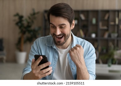 Oh yeah. Euphoric bearded male look at cell screen open mouth read exciting great news receive money present gift online. Overjoyed young male winner raise fist get victory at professional web contest