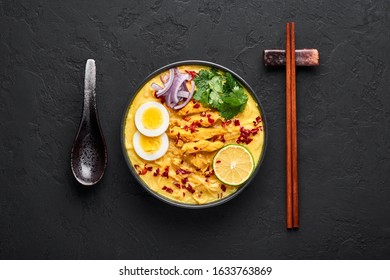 Ohn No Khao Swe in black bowl at dark slate background. Oh No Khao Suey is Coconut Milk Noodle Soup of myanmar cuisine with chicken meat and eggs. Burmese food. Top view