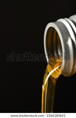 Oil being poured from a plastic jug on a black background. 