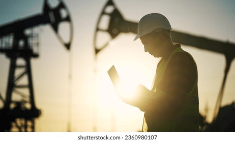 oil business. engineer next to an oil rig. oil production finance concept. gas production. worker with a laptop monitors oil production industry next to an station. a worker in hard hat works