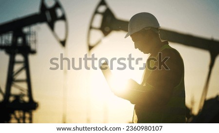oil business. engineer next to an oil rig. oil production finance concept. gas production. worker with a laptop monitors oil production industry next to an station. a worker in hard hat works