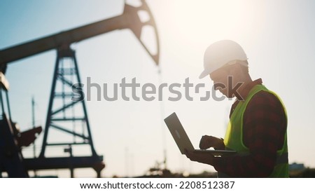 oil business. a worker works next to an oil pump holding a laptop. industry business oil and gas concept. lifestyle engineer studying the level of oil production on a laptop silhouette at sunset Stock fotó © 
