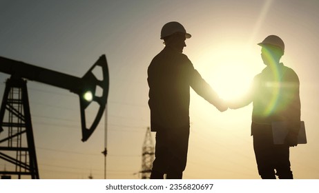 oil business. workers of the fuel industry shaking hands with oil pumps on the lifestyle background. industry business oil and gas concept. engineers of the station handshake silhouette at sunset - Powered by Shutterstock