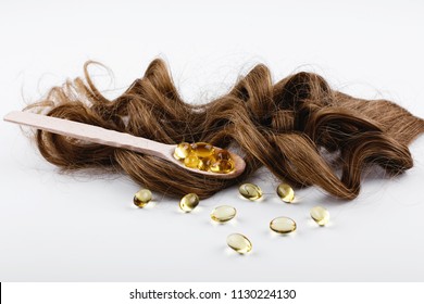 Oil Capsule For Hair With Vitamin E Lie On Wooden Spoon On Brown Hair Curls