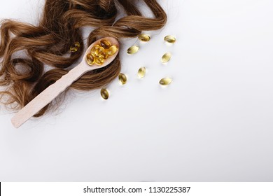 Oil Capsule For Hair With Vitamin E Lie On Wooden Spoon On Brown Hair Curls