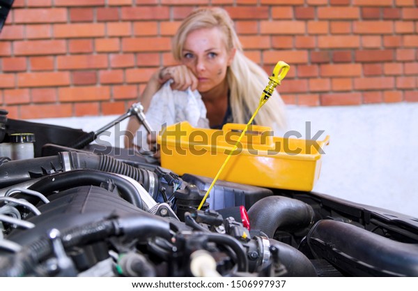 Oil car wire checking in the car service\
and worried young woman mechanic worker thinking about car engine\
problem. Looking under the auto\
hood