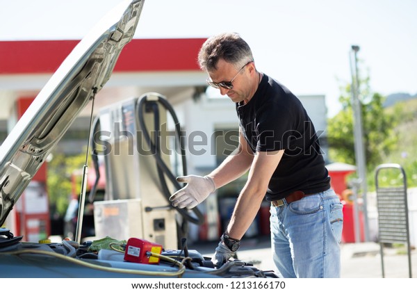 Oil\
change in car. Man repairing the engine in the car. Self-changing\
oil in own car. Man looks under the hood of his\
auto