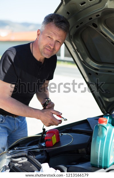 Oil\
change in car. Man repairing the engine in the car. Self-changing\
oil in own car. Man looks under the hood of his\
auto